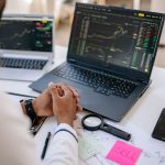 Business professional analyzing stock market data on dual laptops in an office.